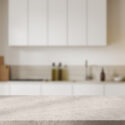 Empty stone countertop on blurred background of beige home kitchen interior, cooking space with refrigerator.